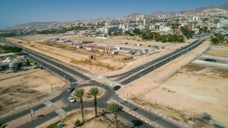 כביש שדה התעופה באילת עם כיכר חדשה ועצי דקל, עבודות סלילה ופיתוח של סמי נופי ובניו על רקע העיר וההרים